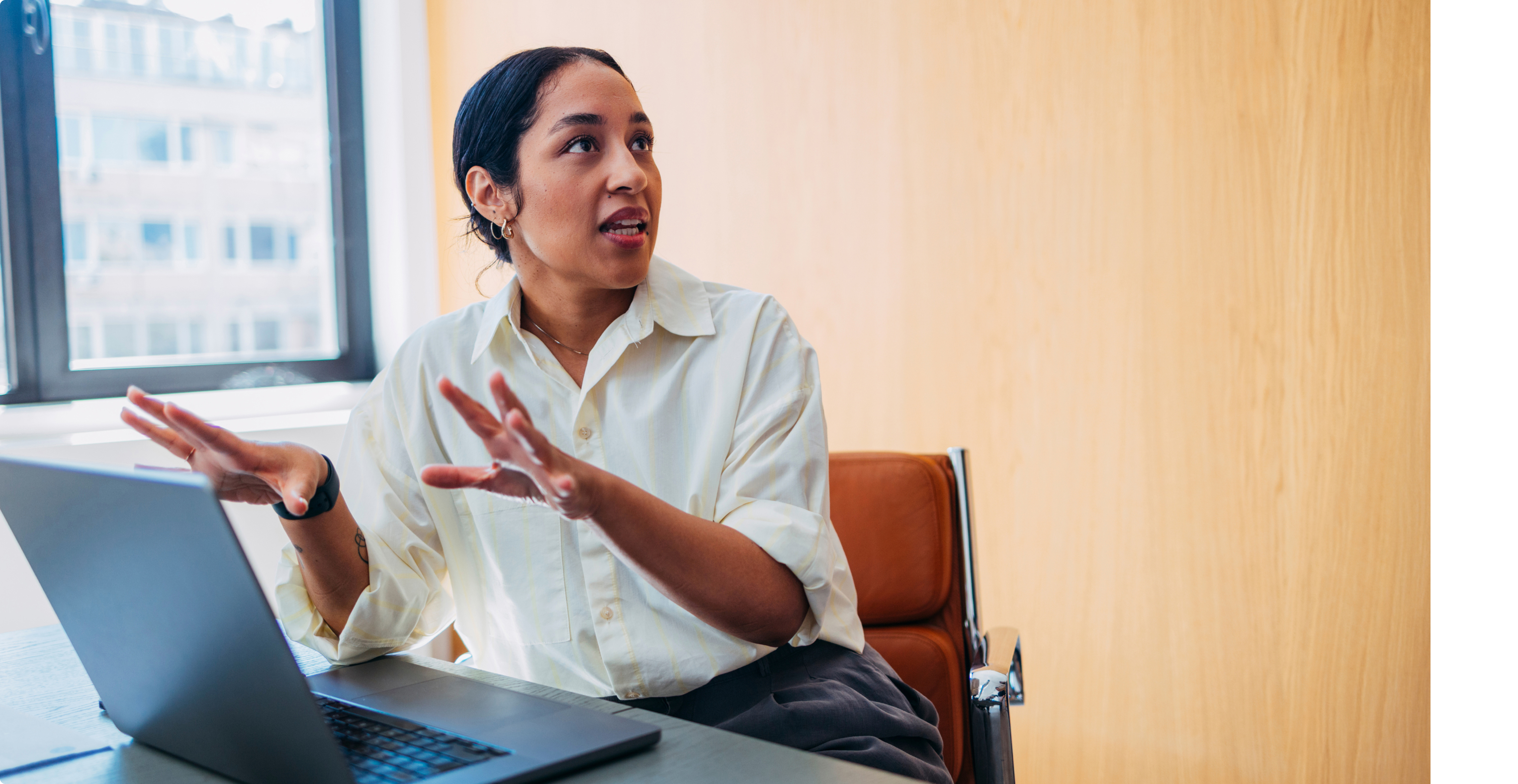 Professional woman gesturing expressively while speaking at a laptop in a modern office