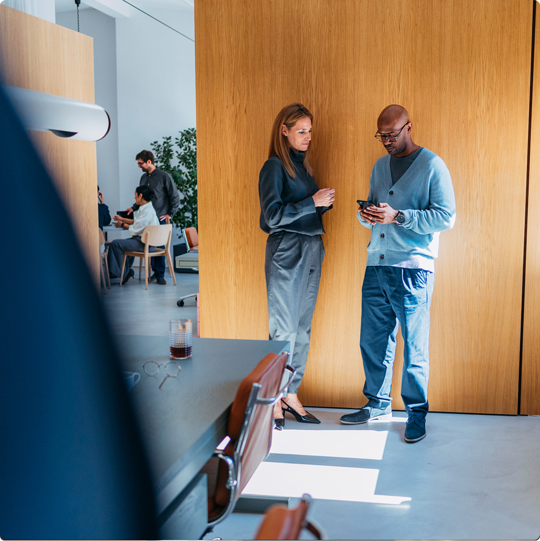 Two colleagues having a discussion while reviewing information on a phone in a modern office